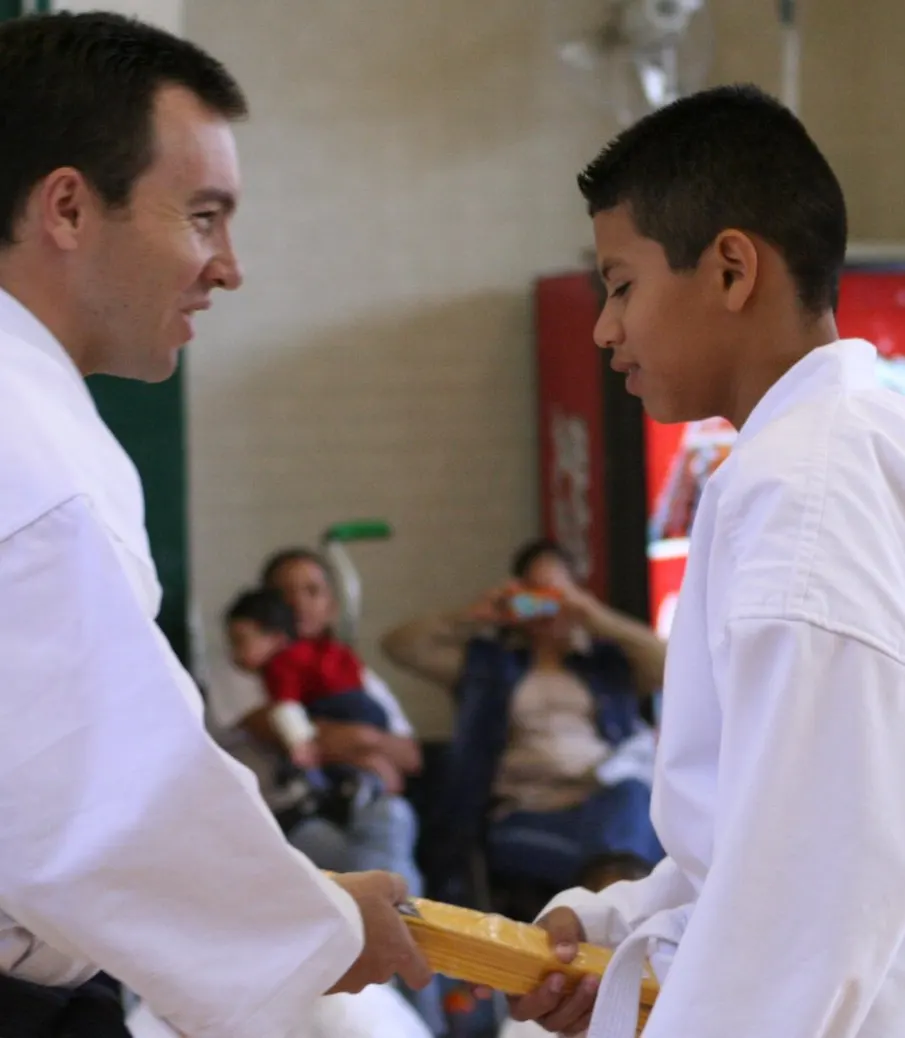 Young instructor presenting a new belt to a boy at a karate promotion ceremony