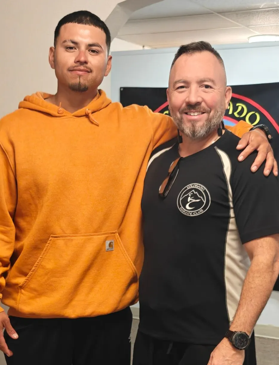 Former student in an orange hoodie posing arm in arm with his instructor years later