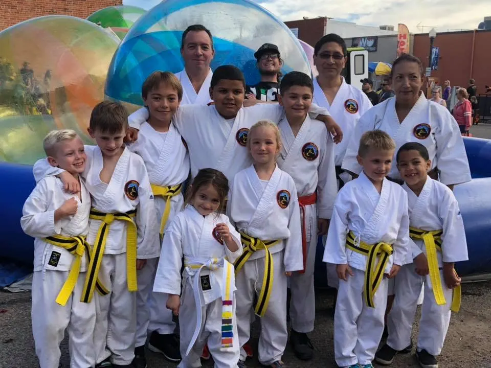 Group of karate students and instructors in white gis posing together at an outdoor street festival