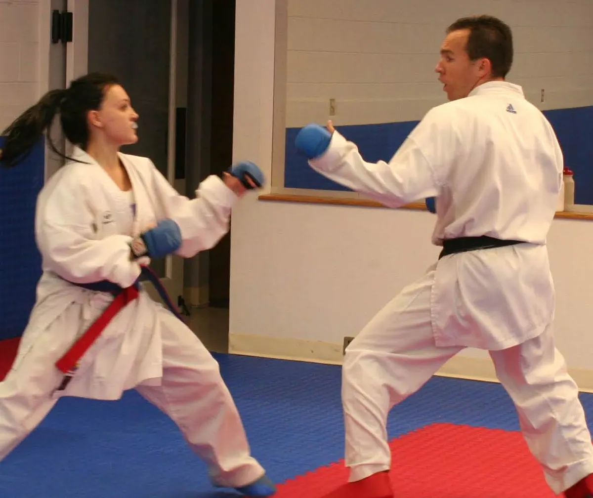 Black belt instructor sparring with a female student wearing blue gloves on a red and blue mat