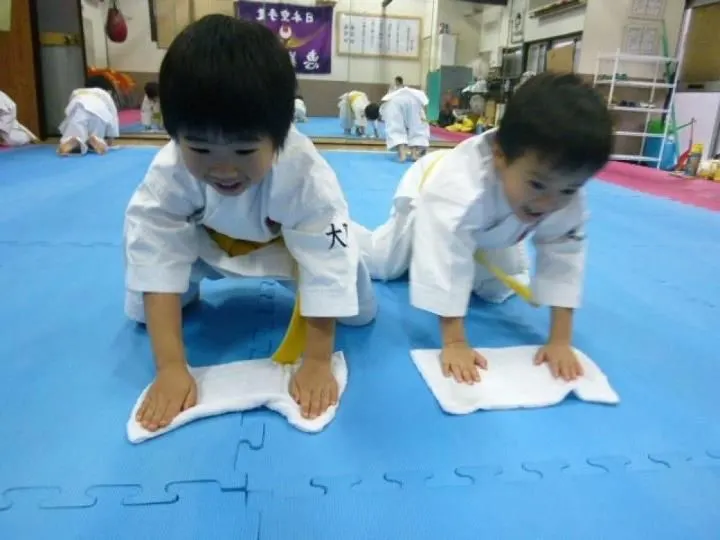 Two young karate students in white gis wiping the dojo mat with towels
